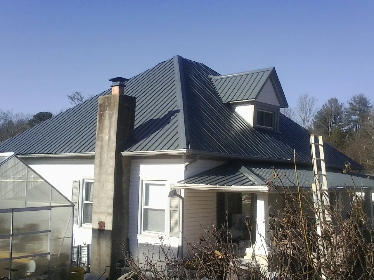Dark blue standing seam metal roof on a white farmhouse with dormer — Slate & Tile Roof Repair by Roofing Brothers in Reed