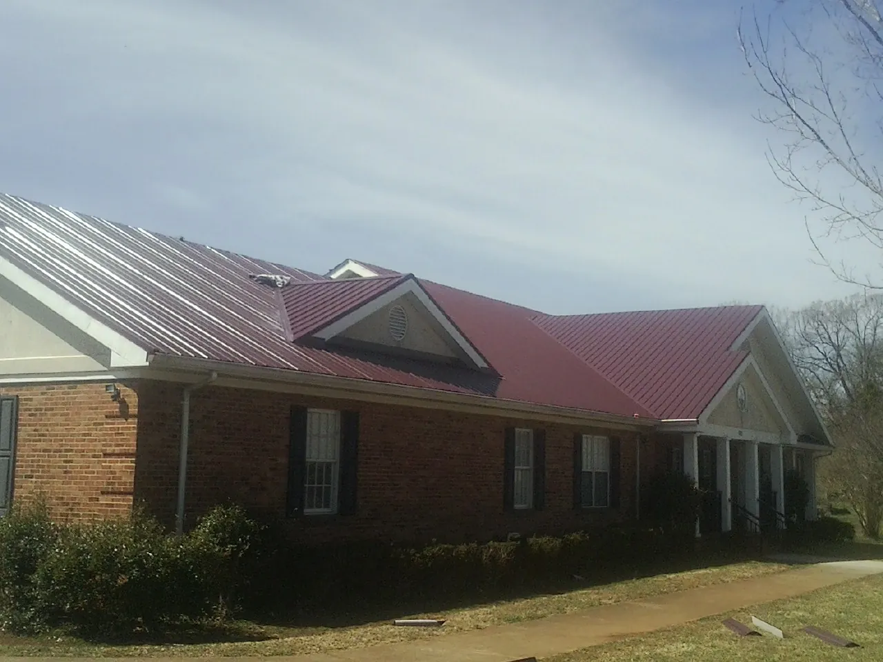 Red metal roof with gabled entries on a long brick building, from a Hail Damage Roof Repair job in Reed