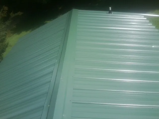 New green metal panels meeting at the ridge of a roof — Flat Roof Repair work by our crew in Reed