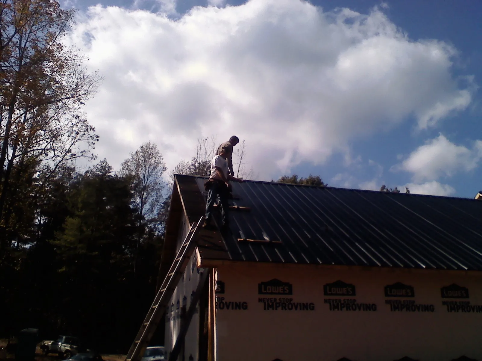 Roofer fastening dark metal panels high against a cloudy sky, from a Roof Inspection job in Reed