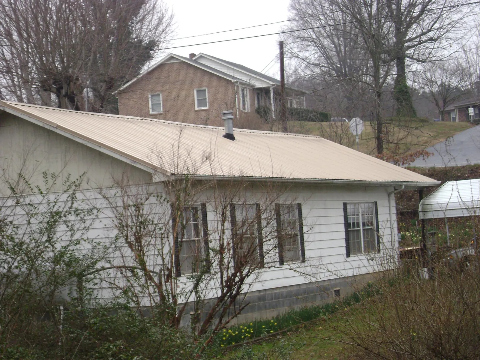 Tan metal roof on a white sided house set into a hillside — Commercial Roofing by Roofing Brothers in Reed