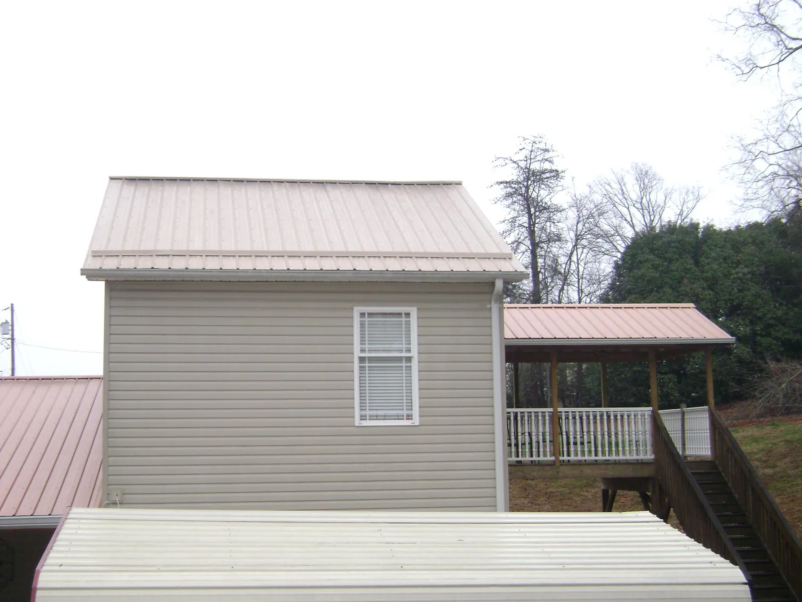 Tan metal roofs on a two story addition and attached porch, from a Roof Replacement job in Reed